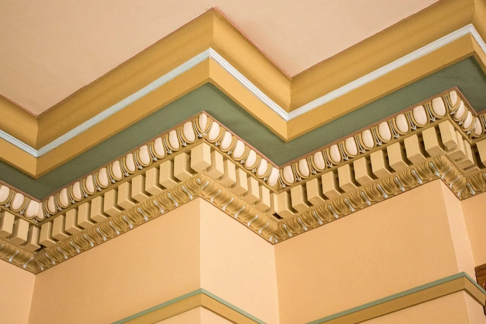 Ornate architectural cornice trim with green, gold, and cream detailing in a building interior.